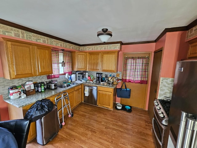 kitchen with hardwood / wood-style floors, appliances with stainless steel finishes, sink, backsplash, and light stone counters