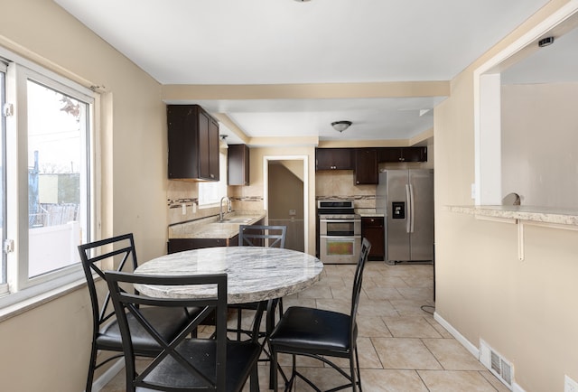 kitchen with stainless steel appliances, sink, light tile patterned floors, a healthy amount of sunlight, and dark brown cabinets