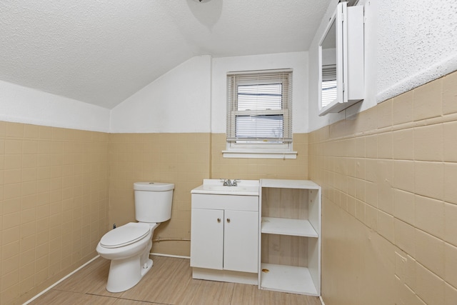 bathroom featuring toilet, a textured ceiling, vaulted ceiling, tile walls, and vanity