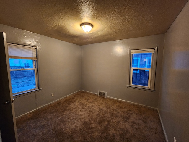 unfurnished room with a textured ceiling, dark carpet, visible vents, and baseboards