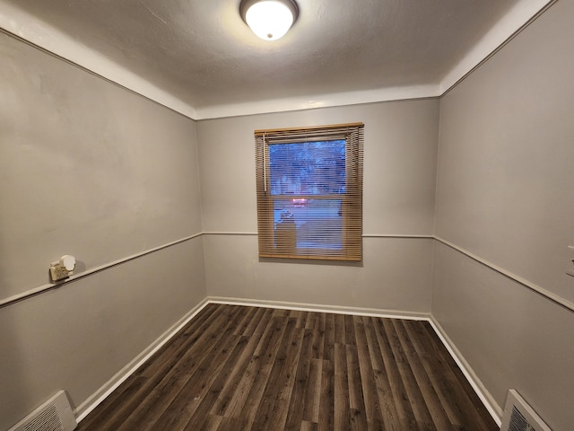 unfurnished room with visible vents, dark wood finished floors, and baseboards