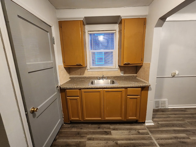 kitchen featuring dark wood finished floors, dark countertops, visible vents, backsplash, and a sink