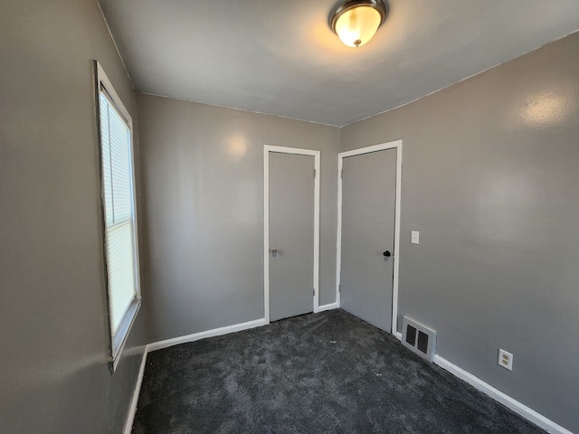 unfurnished bedroom with visible vents, dark carpet, and baseboards