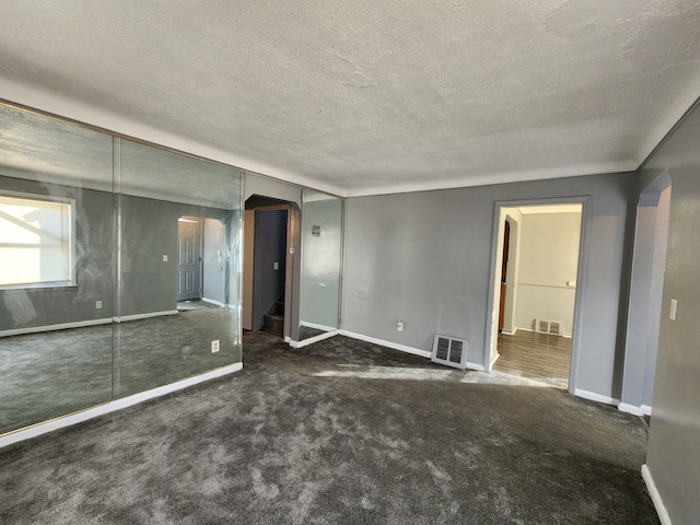 unfurnished bedroom with arched walkways, dark colored carpet, a textured ceiling, and visible vents