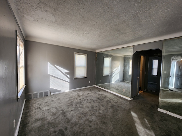 interior space featuring baseboards, visible vents, dark colored carpet, and a textured ceiling