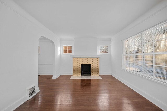 unfurnished living room featuring a brick fireplace, plenty of natural light, dark hardwood / wood-style flooring, and ornamental molding