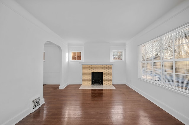 unfurnished living room with a brick fireplace, a wealth of natural light, dark hardwood / wood-style flooring, and crown molding