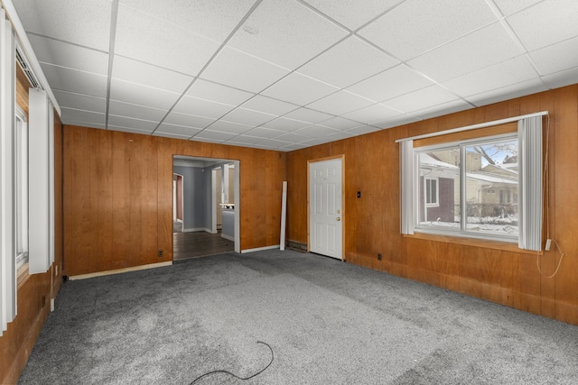 carpeted empty room featuring a drop ceiling and wooden walls