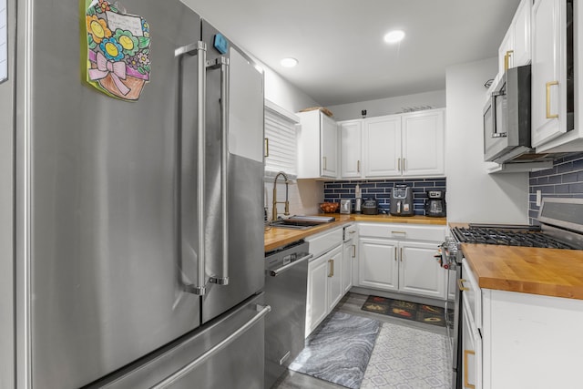 kitchen with stainless steel appliances, sink, butcher block counters, white cabinetry, and decorative backsplash