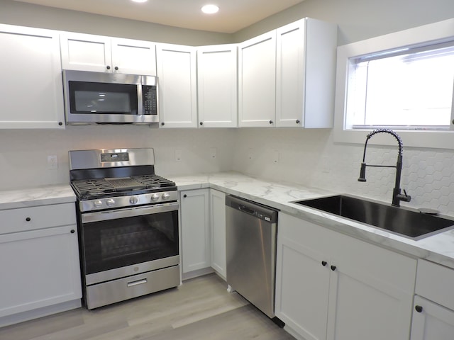 kitchen with white cabinets, appliances with stainless steel finishes, sink, light wood-type flooring, and light stone counters