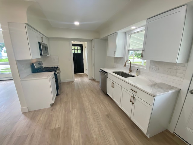 kitchen featuring stainless steel appliances, a healthy amount of sunlight, sink, white cabinets, and tasteful backsplash