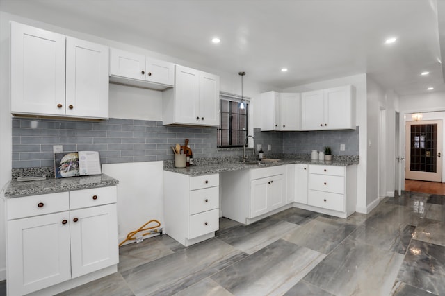 kitchen featuring light stone countertops, white cabinetry, hanging light fixtures, and sink