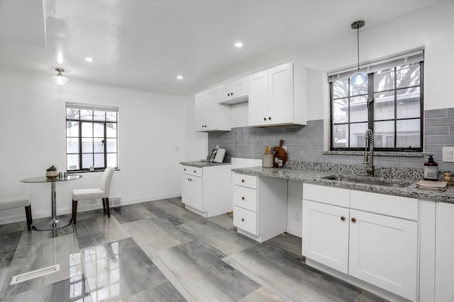 kitchen featuring tasteful backsplash, decorative light fixtures, white cabinets, light stone counters, and sink