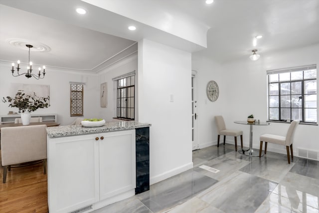 kitchen featuring decorative light fixtures, white cabinetry, light stone countertops, ornamental molding, and a chandelier