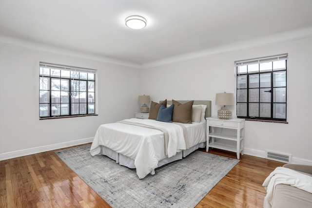 bedroom with wood-type flooring, crown molding, and multiple windows