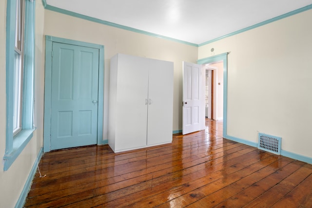 unfurnished bedroom with dark wood-type flooring, ornamental molding, and a closet