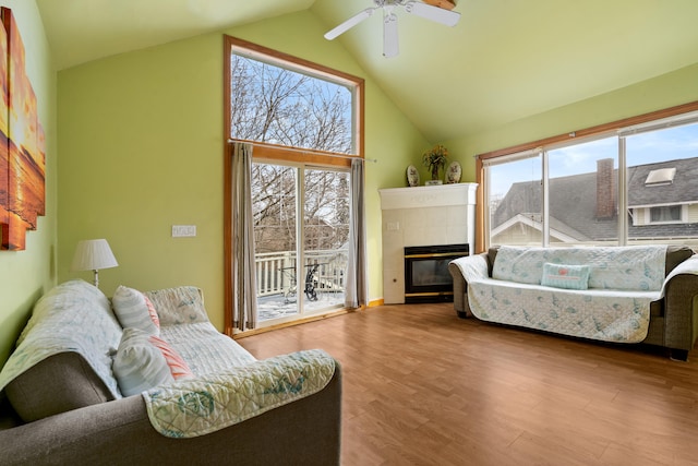 living room with hardwood / wood-style flooring, ceiling fan, high vaulted ceiling, and a tile fireplace