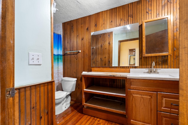 bathroom with wood walls, wood-type flooring, vanity, toilet, and a textured ceiling