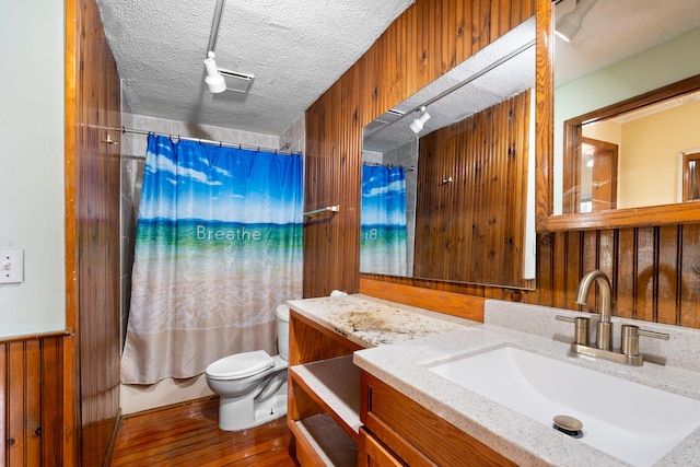 full bathroom with toilet, a textured ceiling, vanity, wooden walls, and hardwood / wood-style floors