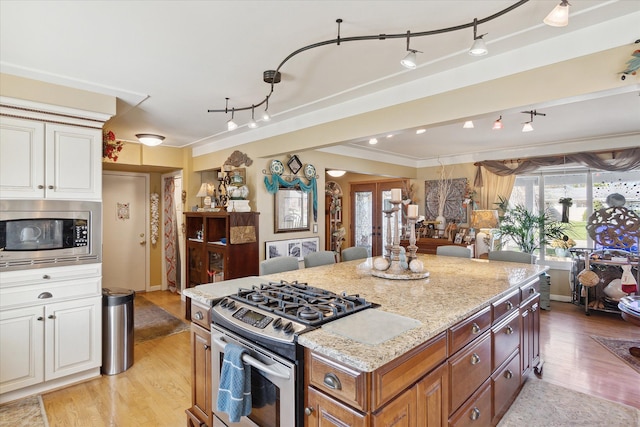 kitchen with appliances with stainless steel finishes, ornamental molding, white cabinets, and light stone countertops