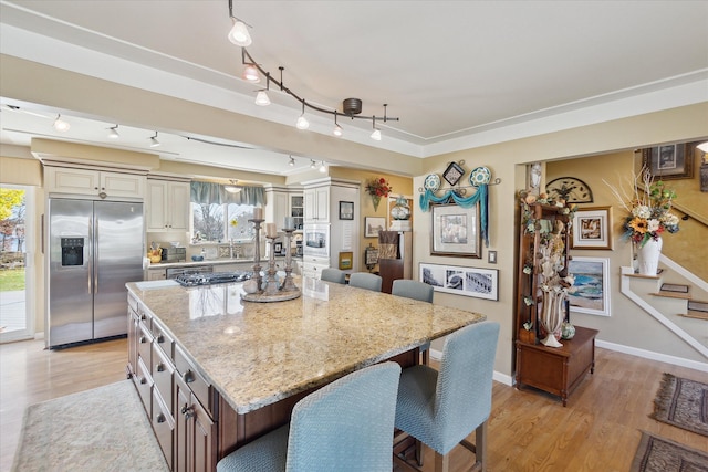 kitchen with light stone countertops, a center island, stainless steel appliances, light wood-type flooring, and a breakfast bar area