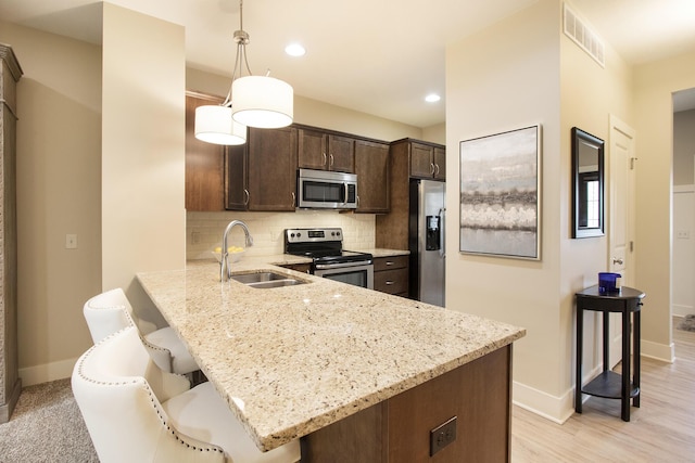 kitchen featuring stainless steel appliances, sink, a breakfast bar area, backsplash, and pendant lighting