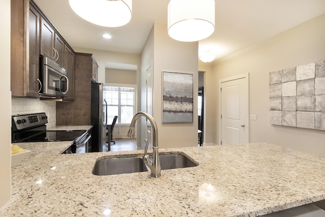 kitchen with sink, tasteful backsplash, kitchen peninsula, light stone countertops, and appliances with stainless steel finishes