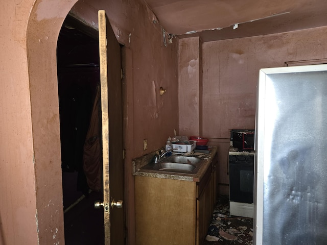 kitchen featuring sink, wood walls, stove, and stainless steel refrigerator