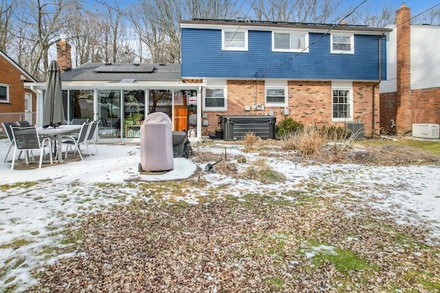 snow covered rear of property featuring a hot tub, central AC unit, and solar panels