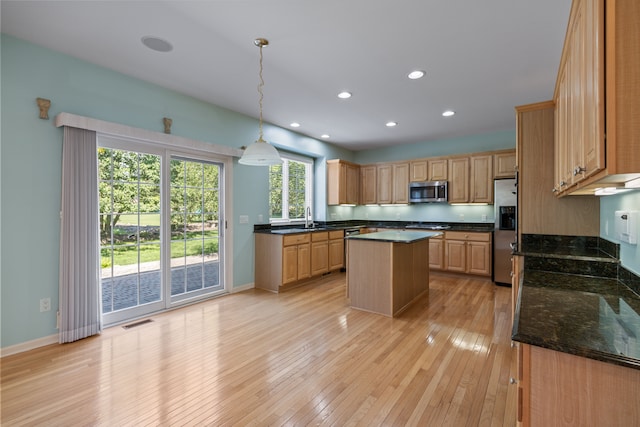 kitchen with appliances with stainless steel finishes, decorative light fixtures, light wood-type flooring, a kitchen island, and sink