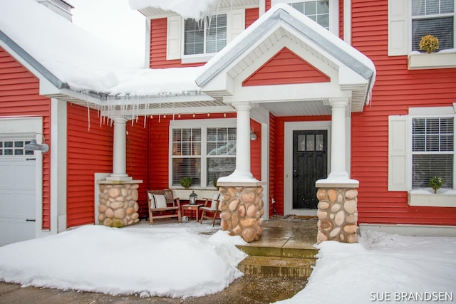 snow covered property entrance with covered porch and a garage