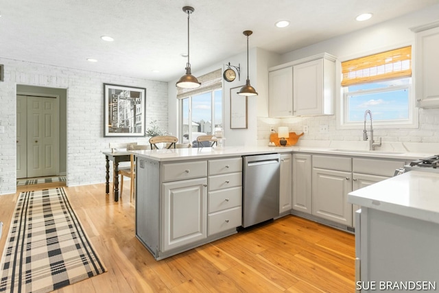 kitchen featuring stainless steel dishwasher, kitchen peninsula, sink, and light hardwood / wood-style floors