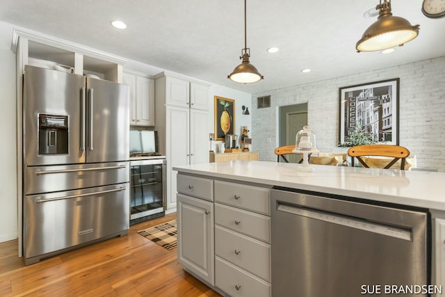 kitchen with decorative light fixtures, appliances with stainless steel finishes, brick wall, and gray cabinets