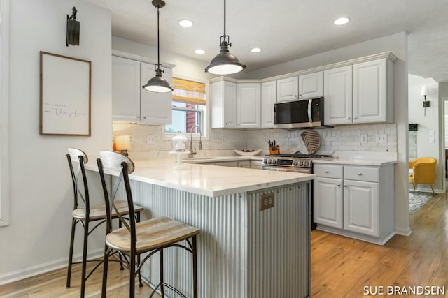 kitchen with white cabinets, kitchen peninsula, stainless steel appliances, and pendant lighting