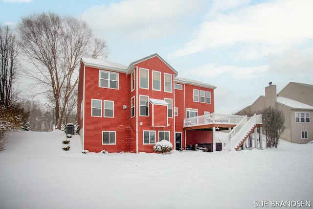 snow covered back of property with cooling unit and a wooden deck