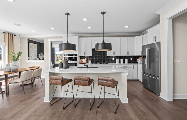 kitchen with pendant lighting, wood-type flooring, white cabinetry, a kitchen island with sink, and stainless steel appliances