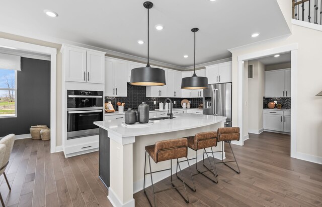 kitchen with decorative light fixtures, white cabinetry, a kitchen island with sink, a breakfast bar, and high end fridge