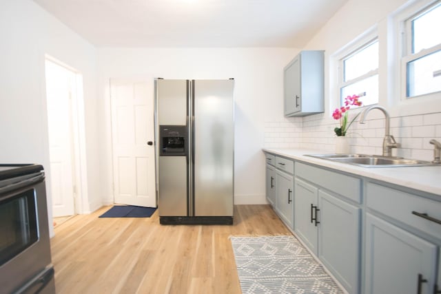 kitchen featuring range, sink, backsplash, stainless steel fridge with ice dispenser, and light wood-type flooring