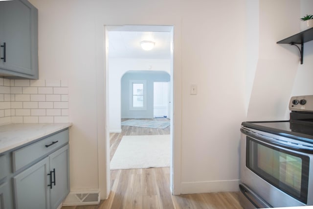 kitchen featuring light hardwood / wood-style floors, gray cabinetry, stainless steel electric range oven, and tasteful backsplash