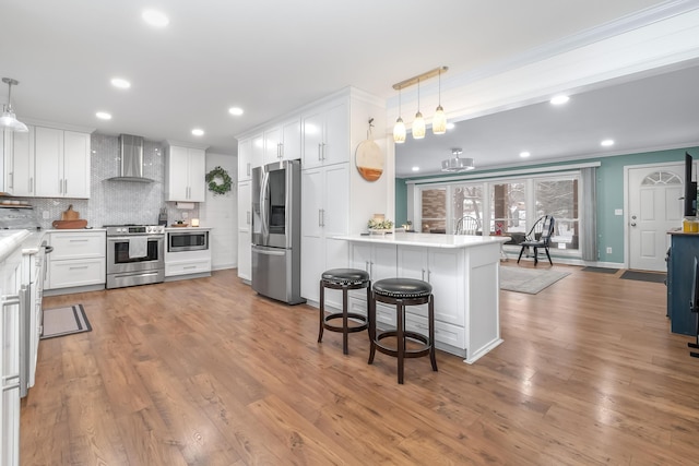 kitchen with wall chimney range hood, kitchen peninsula, white cabinets, and stainless steel appliances