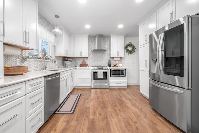 kitchen featuring wall chimney range hood, white cabinets, stainless steel appliances, and hanging light fixtures