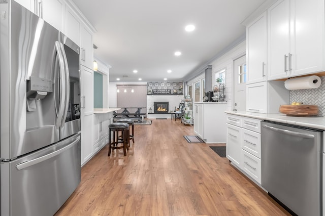 kitchen with white cabinetry, stainless steel appliances, tasteful backsplash, light wood-type flooring, and a fireplace