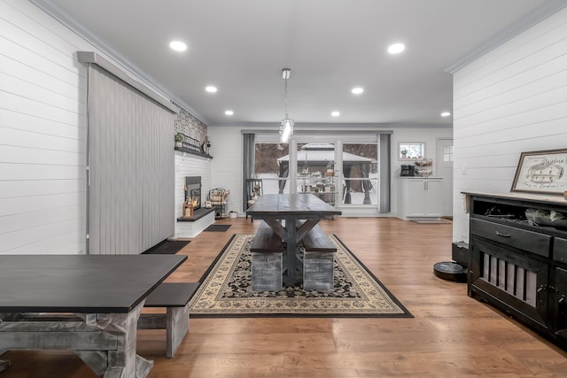 dining room with a fireplace, wooden walls, ornamental molding, and hardwood / wood-style floors