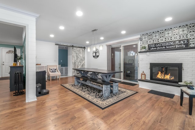 recreation room with a barn door, a fireplace, crown molding, and hardwood / wood-style floors