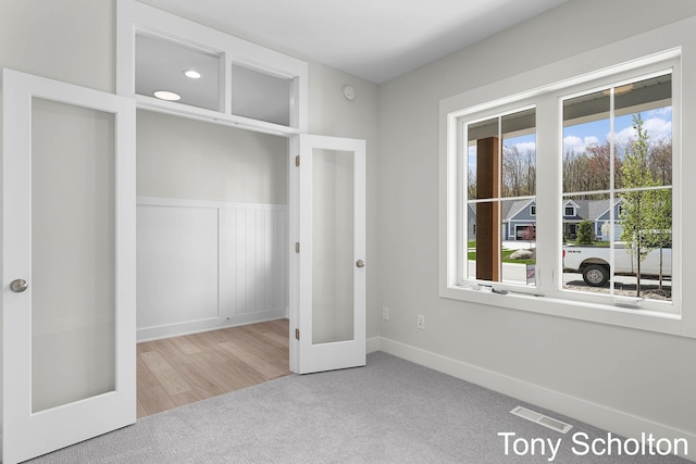 unfurnished bedroom featuring visible vents, carpet floors, a wainscoted wall, and french doors