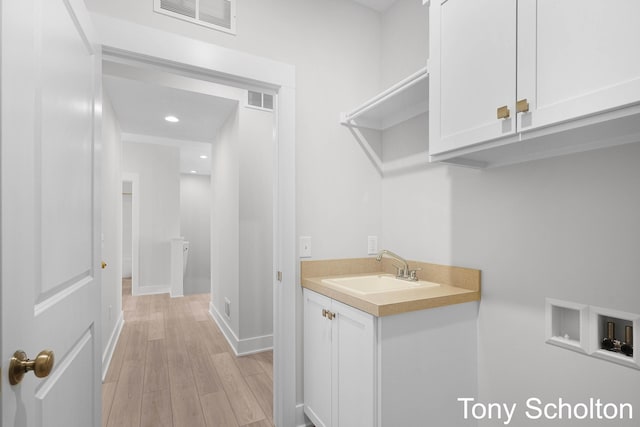 washroom with a sink, washer hookup, light wood finished floors, and visible vents