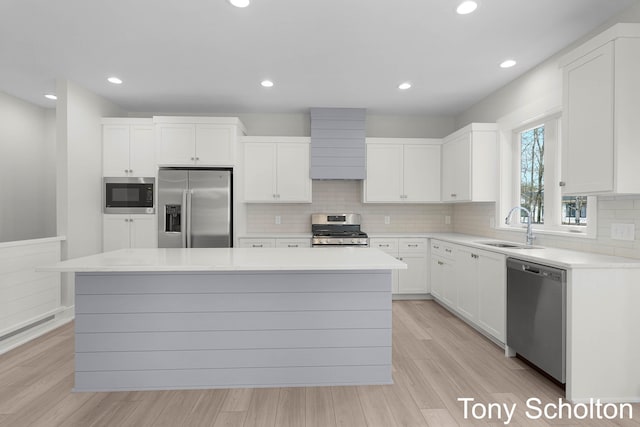 kitchen with a sink, appliances with stainless steel finishes, white cabinets, and light wood-style flooring