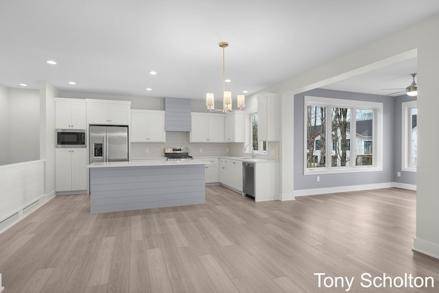 kitchen featuring built in appliances, light countertops, white cabinets, a sink, and light wood-style flooring