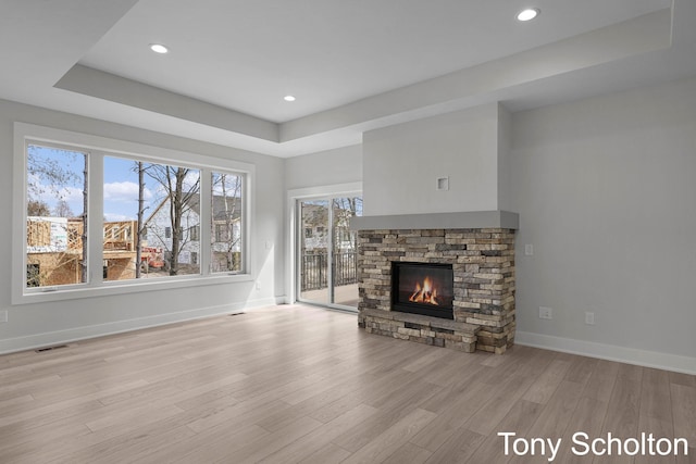 unfurnished living room with visible vents, wood finished floors, a fireplace, baseboards, and a raised ceiling