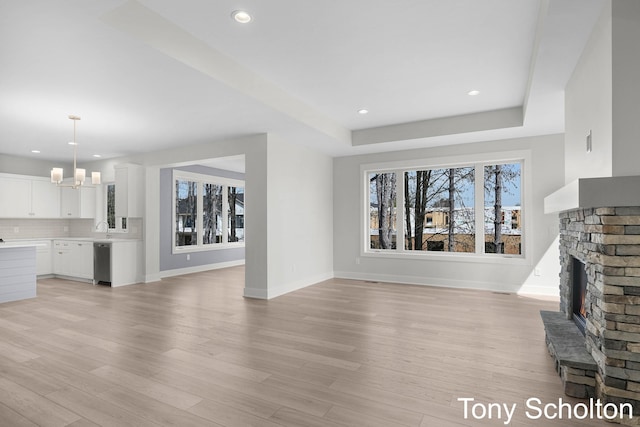 unfurnished living room with light wood-style floors, baseboards, recessed lighting, and a warm lit fireplace